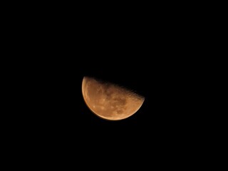 A detailed, reddish half moon shines brightly against the vast, black expanse of space, revealing its cratered surface.