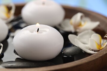 Burning candles, spa stones and orchid flowers in bowl of water, closeup