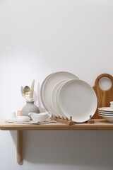 Clean dishware and cutting board on wooden table near white wall