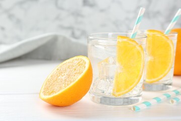 Sparkling water with orange slices in glasses and fresh fruit on white wooden table, closeup