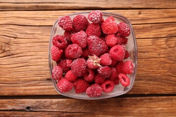 Ripe frozen raspberries in bowl on wooden table, top view