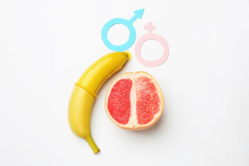 Sex education. Banana with condom, grapefruit, paper female and male gender symbols on white...
