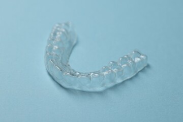 One clear aligner on light blue background, closeup