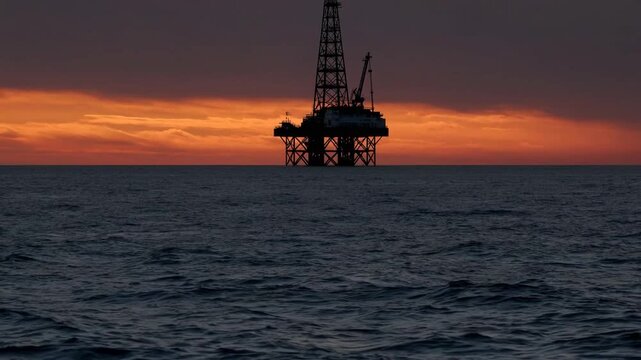 Outline of offshore petroleum extraction platform on the ocean against vivid sunset sky