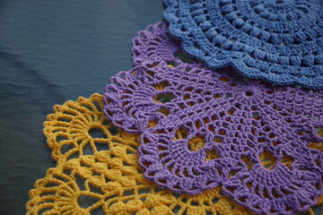 Colorful handmade crochet doilies in blue, purple and yellow on a glass surface.
