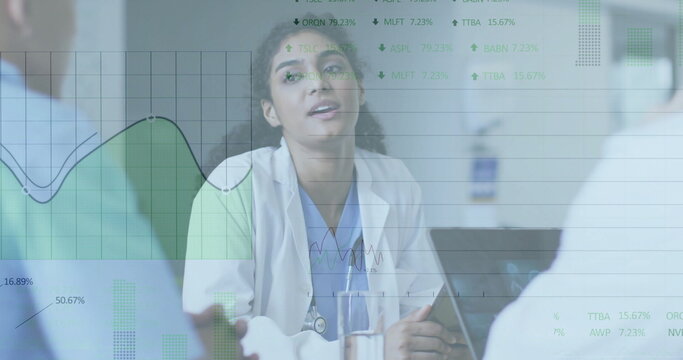 Doctor with stethoscope reviewing data with team in hospital meeting room, with laptop, water glass