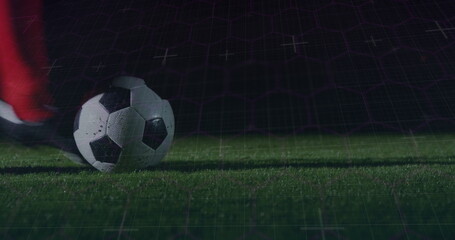 Resting classic soccer ball beneath red sock and black cleat on night pitch, with digital grid