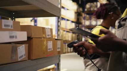 African american e-commerce employee scanning awb tracking numbers, registering shipping labels and details for the warehouse inventory records. Handling pallets import export operations. Camera A. - Powered by Adobe