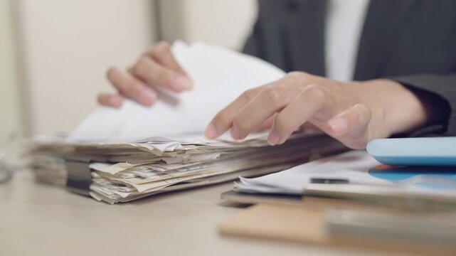 Close-up of a woman sorting through a thick pile of office documents, showcasing the workload and administrative duties in a modern corporate environment.