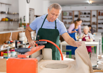Old man rolling piece of clay on special mechanical machine - craft machine clay press roller