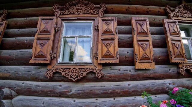 Close-Up Detail of the Ornate Rustic Wooden Window Frames with Hand-Carved Decorations on Traditional Russian Log Cabin, Surrounded by Flower Bed Travel