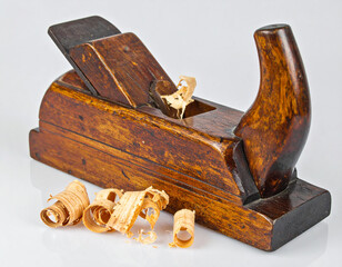 A worn wooden carpenter's plane sitting on a white surface with several wood shavings.