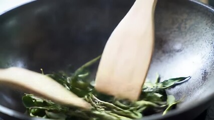 Close Up Shot of Person Stirring Green Curry Leaves in Black Wok with Wooden Spatula Perfect for Cooking Ads and Promotional Material for National Curry Day and Other Culinary Occasions