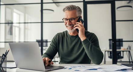 Smiling businessman working on laptop and talking on phone