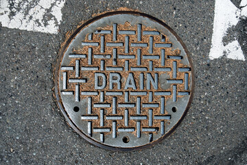 Round iron sewar utility drain access point lid in a asphalt street with orange pine needles on it
