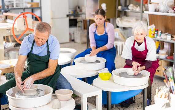 gray-haired potter works on potter's wheel to create clay vase