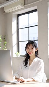 若い日本人女性が白いブラウスを着てデスクトップパソコンに向かう様子を捉えたフォトリアルなイメージ。髪はゆるやかに波打ち、片側に分けられています。背景はマットな漆喰壁と小さな四角窓、デスクの隅には小さな観葉植物。柔らかな自然光が窓から差し込み、落ち着いた雰囲気を演出しています。