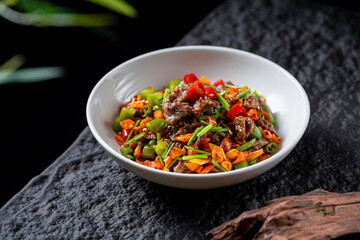 A delicious stir-fried dish with various vegetables and meat served in a white bowl, showcasing vibrant colors and appetizing appearance.
