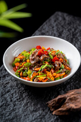 A delicious stir-fried dish with mixed vegetables and meat served in a white bowl, showcasing vibrant colors and appetizing appearance.