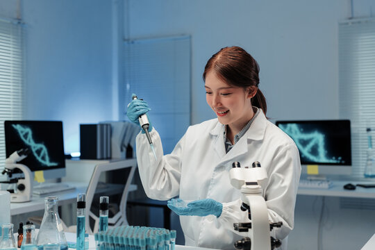 Asian female scientist in lab coat using micropipette dropping blue liquid into petri dish for experiment in laboratory