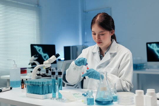 Scientist wearing lab coat and gloves preparing blood sample test in modern laboratory with microscope and dna structure on computer screen