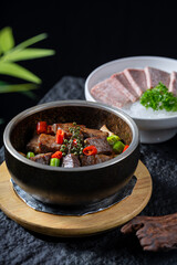 A stone pot with braised beef and colorful vegetables, accompanied by sliced meat in the background, presenting a delicious culinary scene.