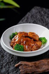 Braised pork slices in rich sauce are served with broccoli in a white bowl, presenting a delicious and appetizing dish.