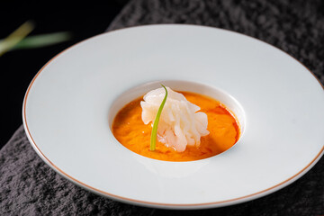 A gourmet appetizer featuring orange sauce with shrimp slices, presented elegantly in a white plate.