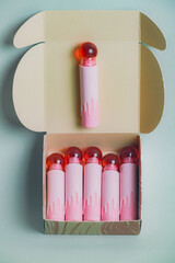 Open box of pink lipsticks aligned in a row with a glossy pink sphere center; elegant packaging and...
