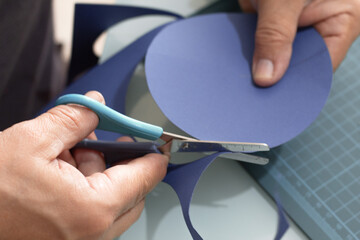 Hand cutting circles out of blue cardboard with scissors on a cutting board, the first step in...