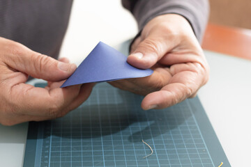 An adult's hands holding a circular piece of blue paper folded to create a handmade cone