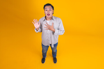 Asian Man Feeling Shocked and Surprised with Hand on Chest Isolated on Yellow Background