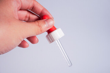 Hand holding pipette with red lid isolated on horizontal copy spaced plain background.