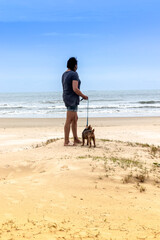 Woman and dog gazing at the ocean from a sand dune. Serenity and connection with nature