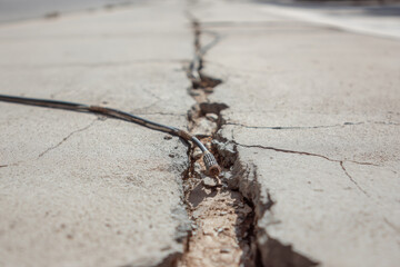 Deep crack in urban pavement revealing damaged underground cable, causing concern