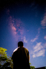 Back view of a person silhouetted against a beautiful night sky filled with stars and the vibrant...