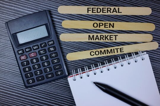A financial concept displayed with a calculator, notepad, and labeled wooden sticks spelling Federal Open Market Committee.
