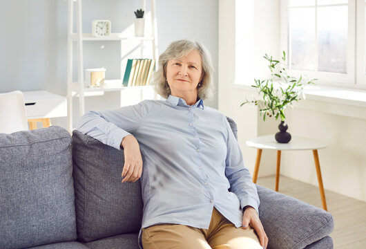 Retired old senior woman, attractive gray hair elderly person, happy healthy middle aged woman sitting on comfortable couch at home. Grandmother, positive single senior retired female in living room