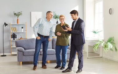 Male real estate agent or realtor guides a senior couple through a new property or apartment,...