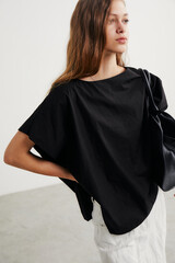 Teen girl in a black oversized top with a casual pose in a minimal indoor setting.