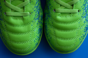 A pair of soccer cleats in a vibrant green color, decorated with blue paint splatters. The front...