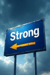 Obraz premium A weathered blue road sign points left, displaying the word Strong in bold white lettering, vertical composition. The contrasting yellow arrow and dramatic sky create a powerful visual statement.