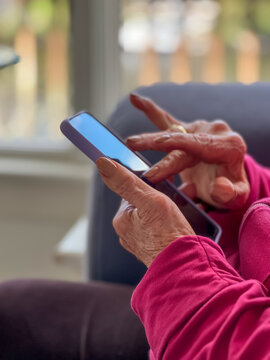 Closeup of elderly senior woman's hands using technology while scrolling down her mobile device. 