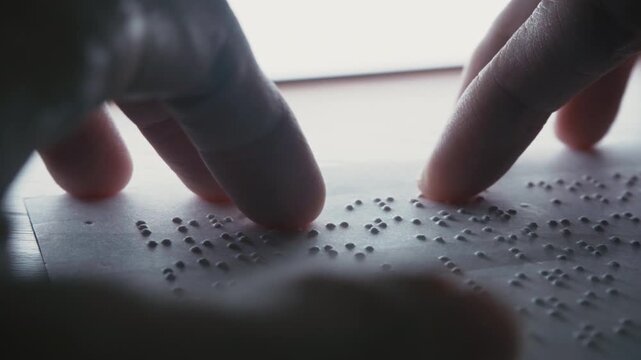Visually impaired people use their fingertips to read Braille on paper, which displays dummy Lorem ipsum text. - Powered by Adobe