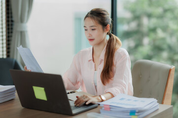 Professional Asian woman committed to her work, surrounded by office documents and computer.