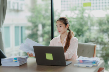 Professional Asian woman committed to her work, surrounded by office documents and computer.