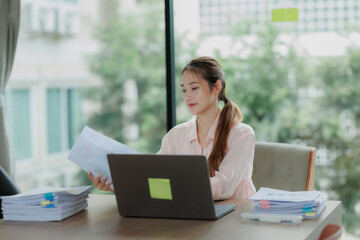 Professional Asian woman committed to her work, surrounded by office documents and computer.