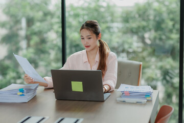 Professional Asian woman committed to her work, surrounded by office documents and computer.