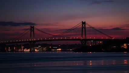 Fototapeta premium Silhouetted suspension bridge at dusk with city lights