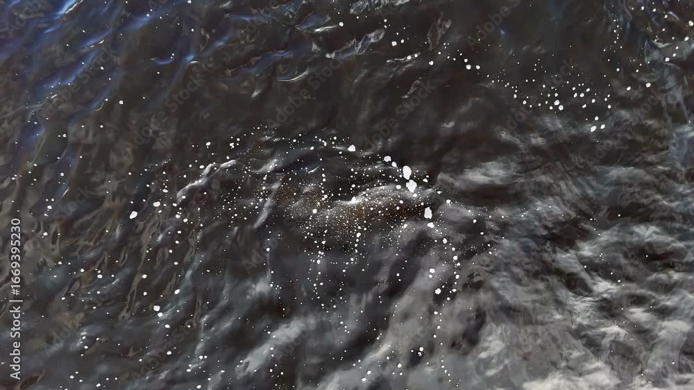 Poster aerial view of bubbling floodwaters flowing over dark terrain. surface foam and ripples indicate tur